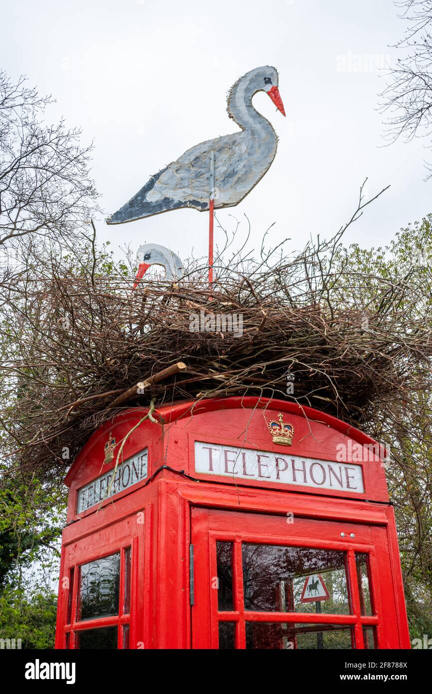 Caja de teléfono roja decorada para Semana Santa con un nido de cigüeñas artificiales en la parte superior, Compton Village, Surrey, Inglaterra, Reino Unido Foto de stock