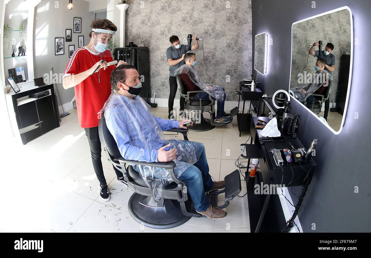 Luke Nancollis (izquierda) corta el pelo de John-Paul Jeffs en la reapertura de la peluquería de caballeros Crate en Knutsford, Cheshire, mientras Inglaterra da otro paso atrás hacia la normalidad con la mayor relajación de las restricciones de cierre. Fecha de la foto: Lunes 12 de abril de 2021. Foto de stock