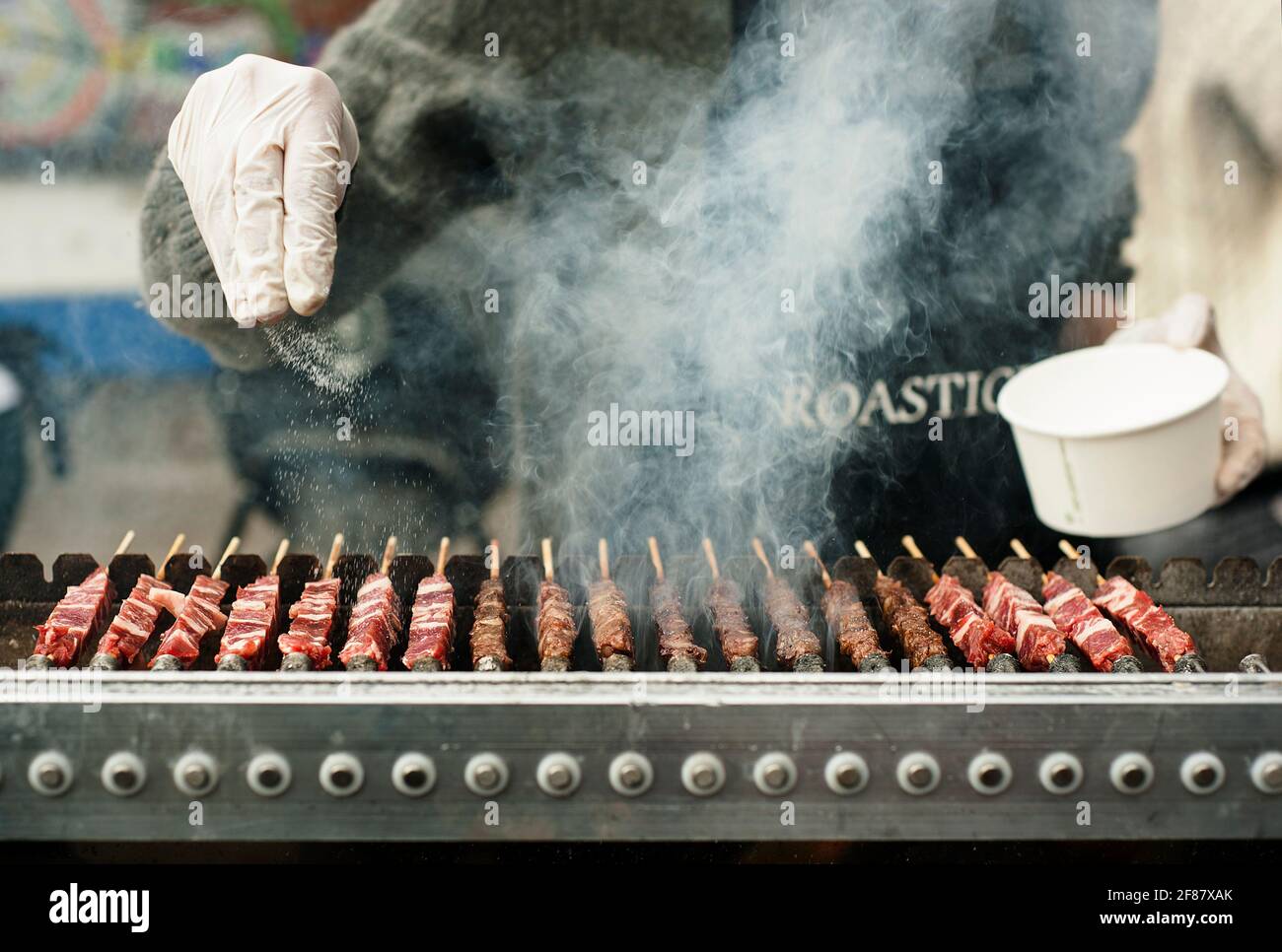 Primer plano de las manos saltando brochetas estilo kebab. Asado de carne en parrilla en un mercado de comida emergente. Brick Lane, Londres, Reino Unido. Abr 2014 Foto de stock