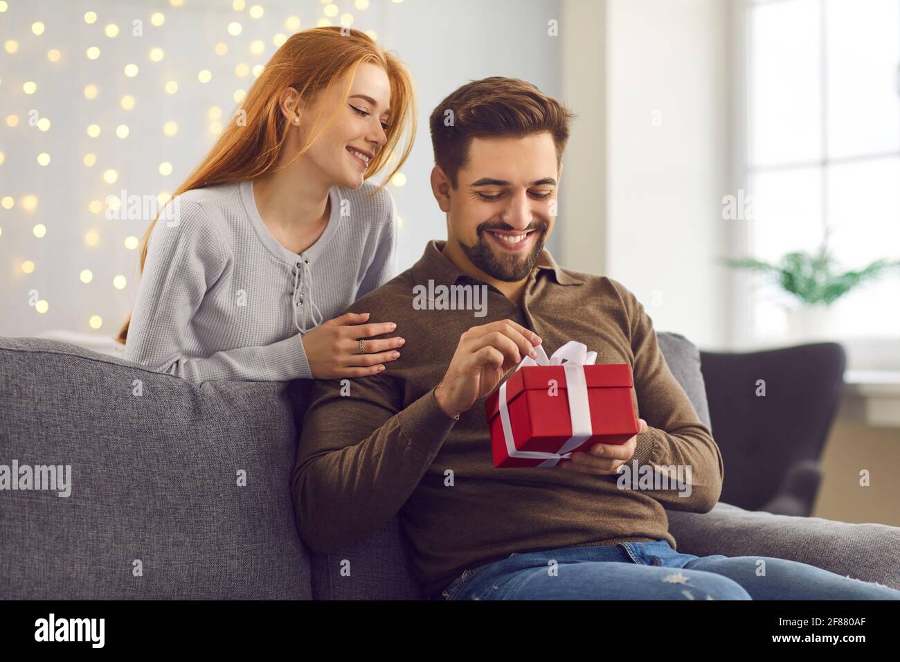 Joven hombre feliz novio abriendo la caja de regalo de su amante novia sonriente Foto de stock