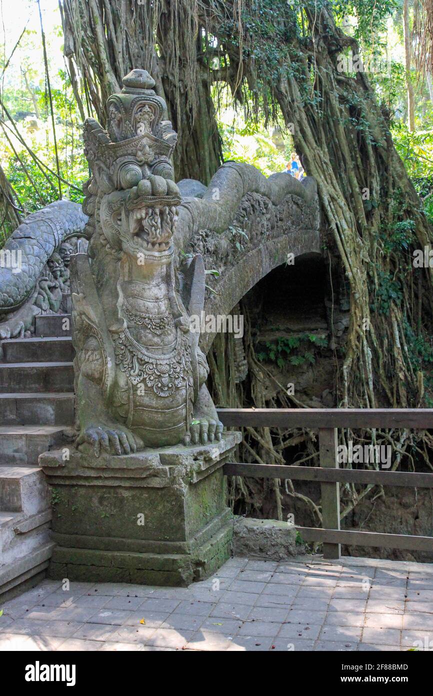 Tradicional dragón de piedra tallada que protege el puente peatonal en el bosque de monos en Ubud, Bali, Indonesia Foto de stock