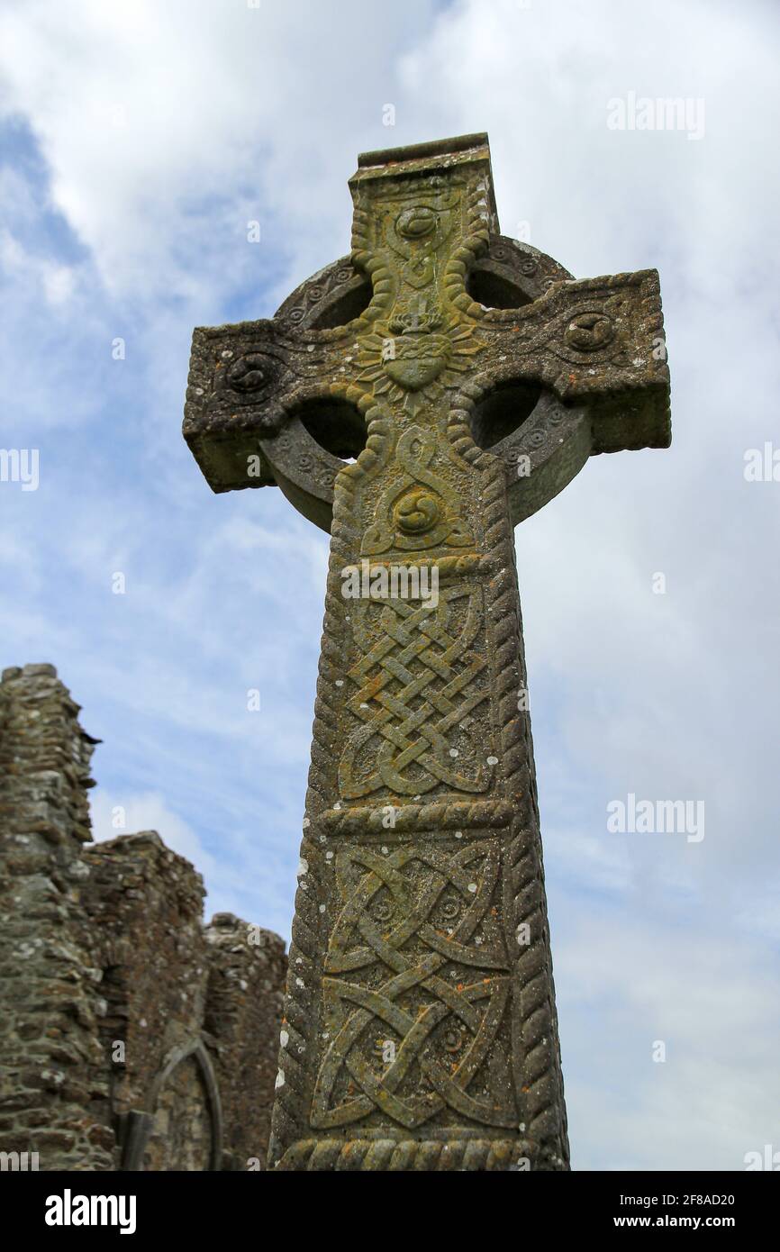 Cruz Celta de Piedra Verde Mossy con corazón de piedra tallada con Ruinas de piedra contra el cielo azul nublado en Irlanda Foto de stock
