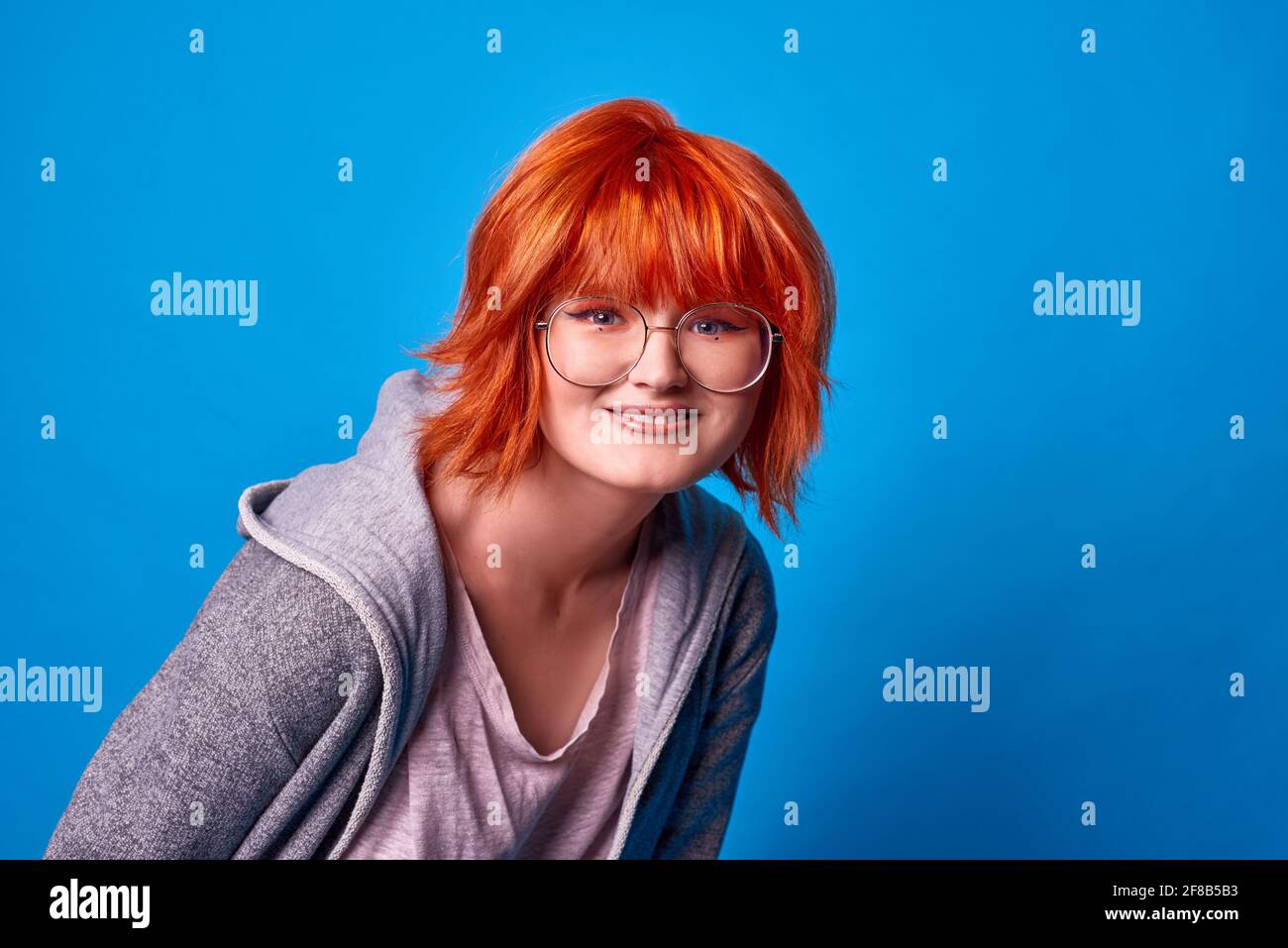chica feliz con su corte de pelo rojo sobre fondo azul. hipster chica en  vasos redondos estilo harry potter Fotografía de stock - Alamy
