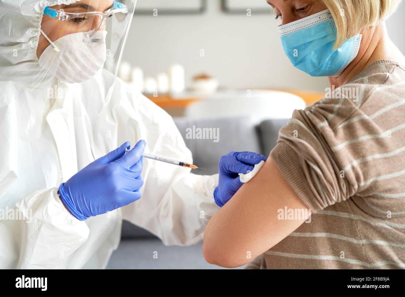 Médico en una visita domiciliaria que le da una vacuna a la persona mayor paciente Foto de stock