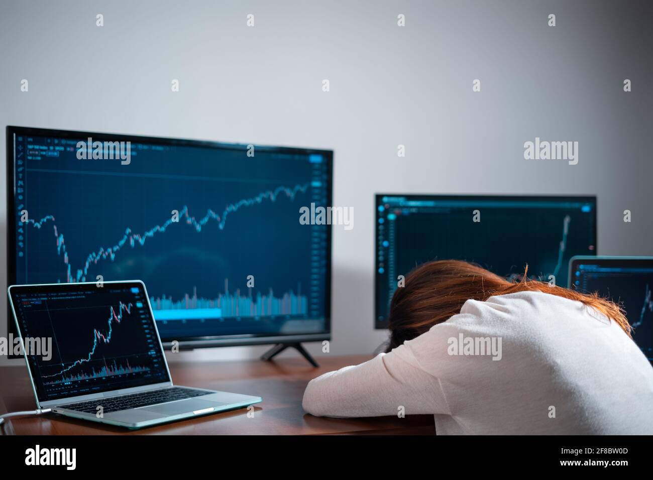 mujer cansada comerciante principiante durmiendo cerca del monitor con gráfico de valores en el lugar de trabajo Foto de stock