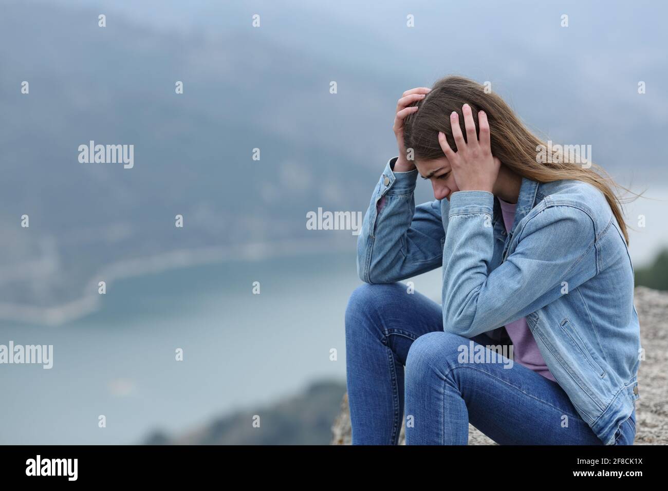 Triste adolescente quejándose sentado solo en un acantilado en el montaña Foto de stock