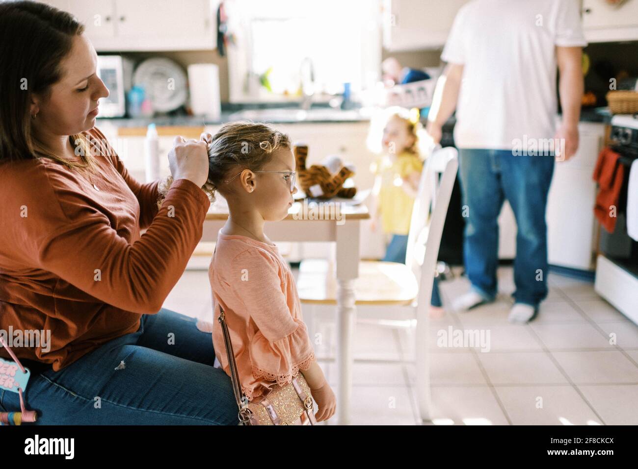 Niña de edad preescolar que consigue el pelo hecho por su madre en la cocina Foto de stock