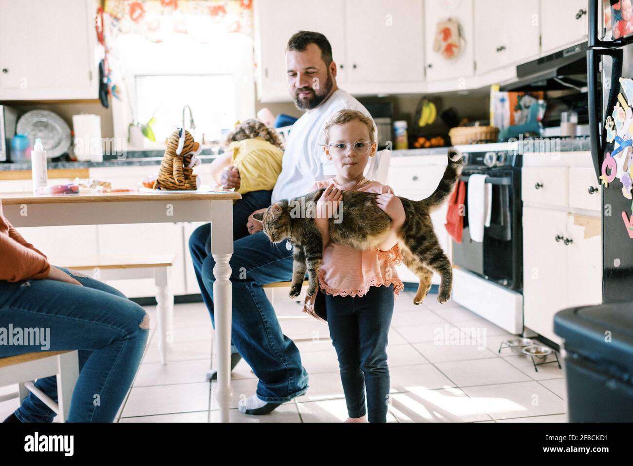 Pequeña niña sosteniendo su lindo gato mascota en ella brazos en la cocina Foto de stock