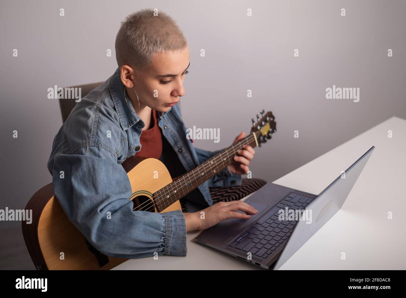La joven está aprendiendo a tocar la guitarra en línea. Lecciones de música  a distancia en un portátil Fotografía de stock - Alamy