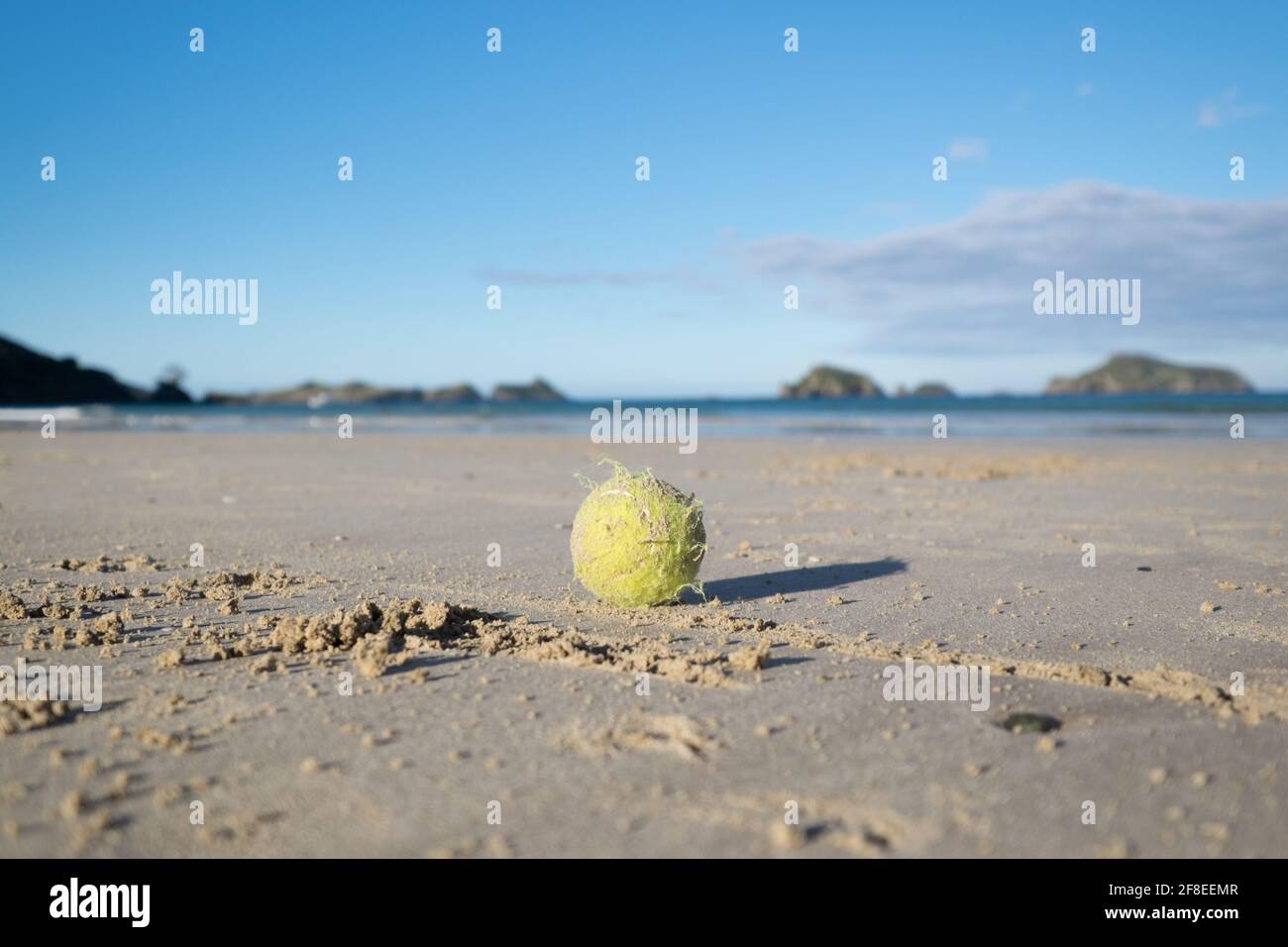 Antigua pelota de tenis de arena en una playa de Nueva Zelanda, con poca profundidad de campo y cielo azul Foto de stock