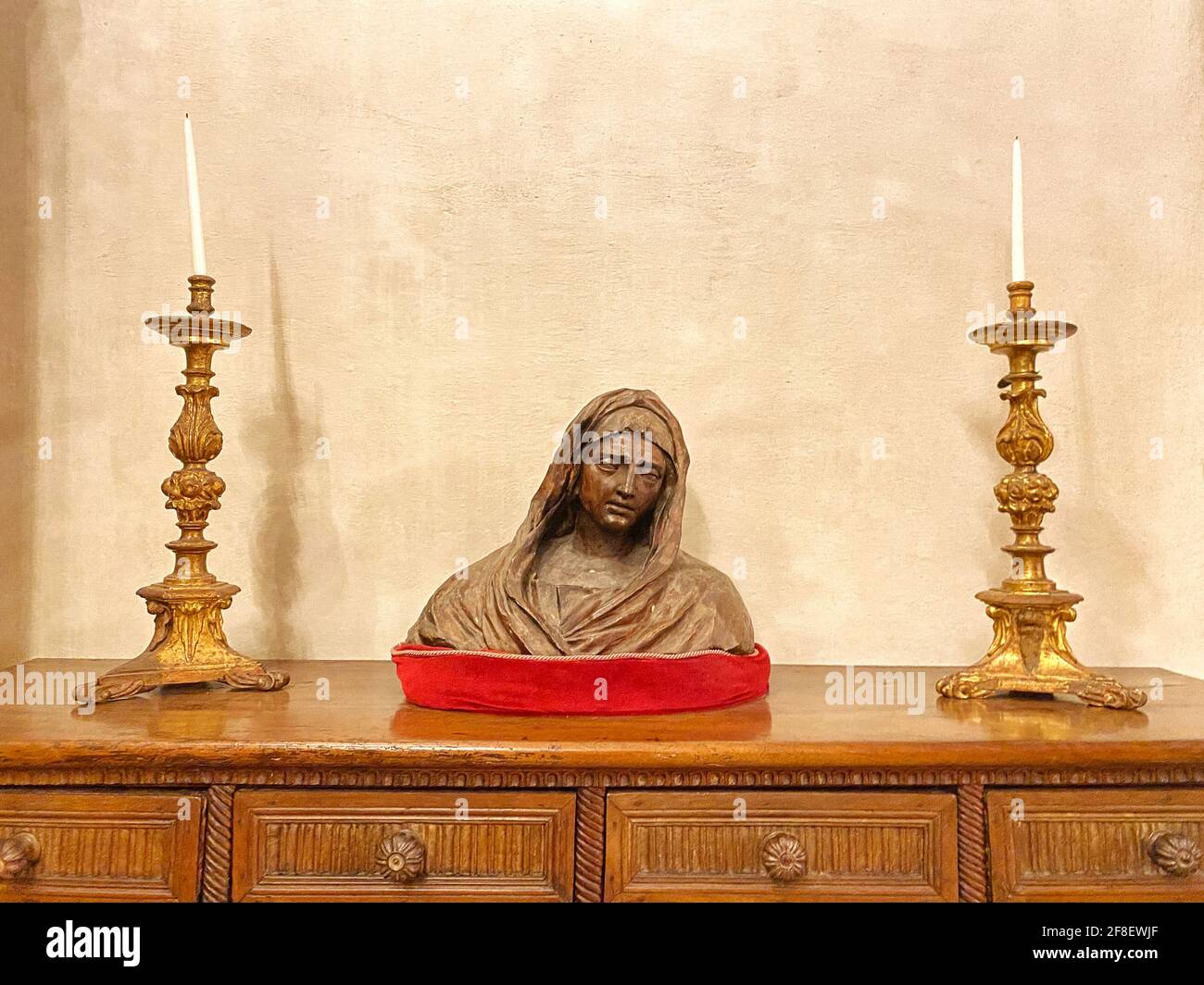 Escultura de la Virgen María, estatua sobre una mesa de madera rodeada por dos largas velas doradas. CopySpace para texto Foto de stock