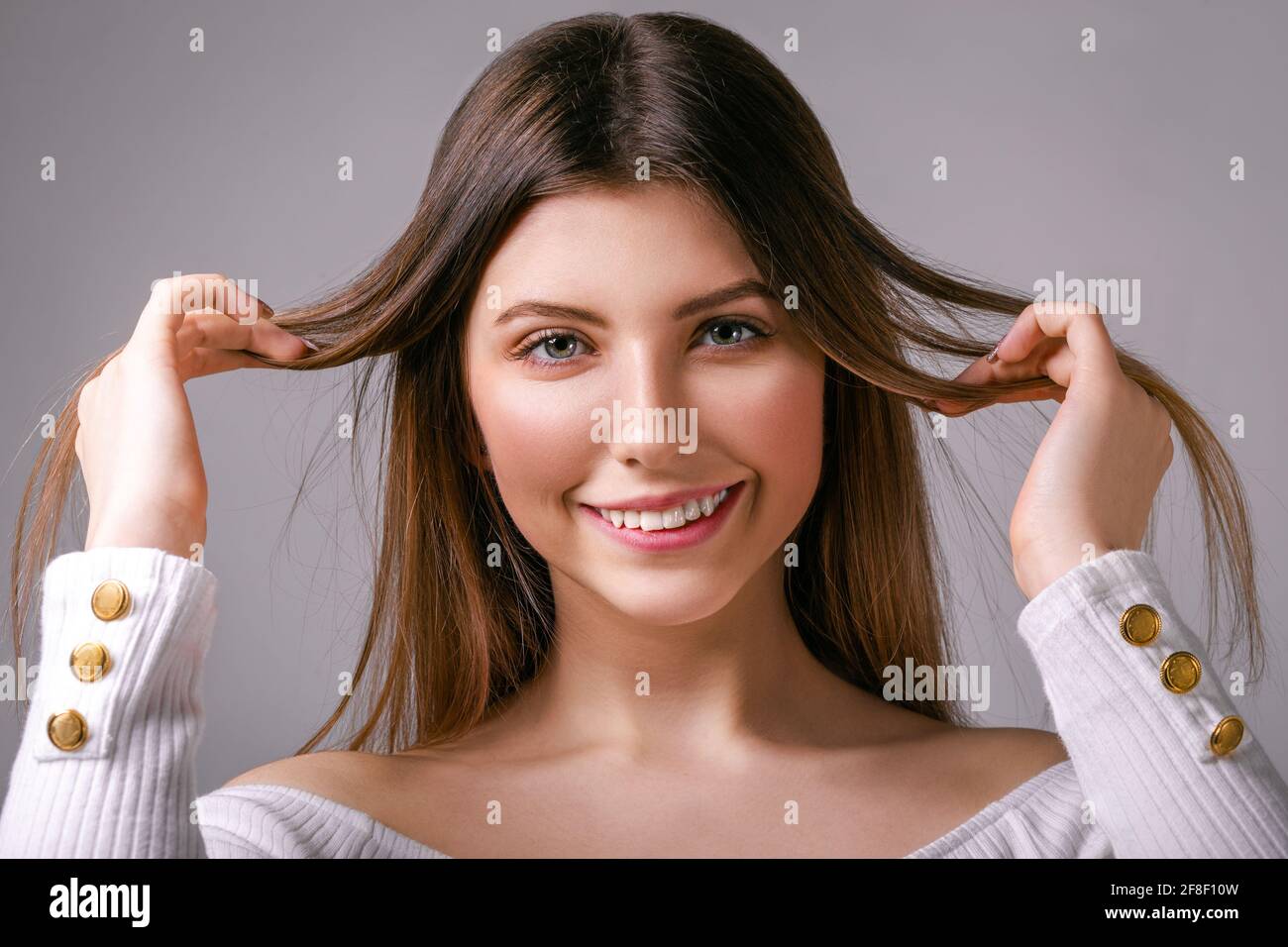 Chica joven encantada con el pelo suelto se coloca en un gris aspecto de fondo Foto de stock