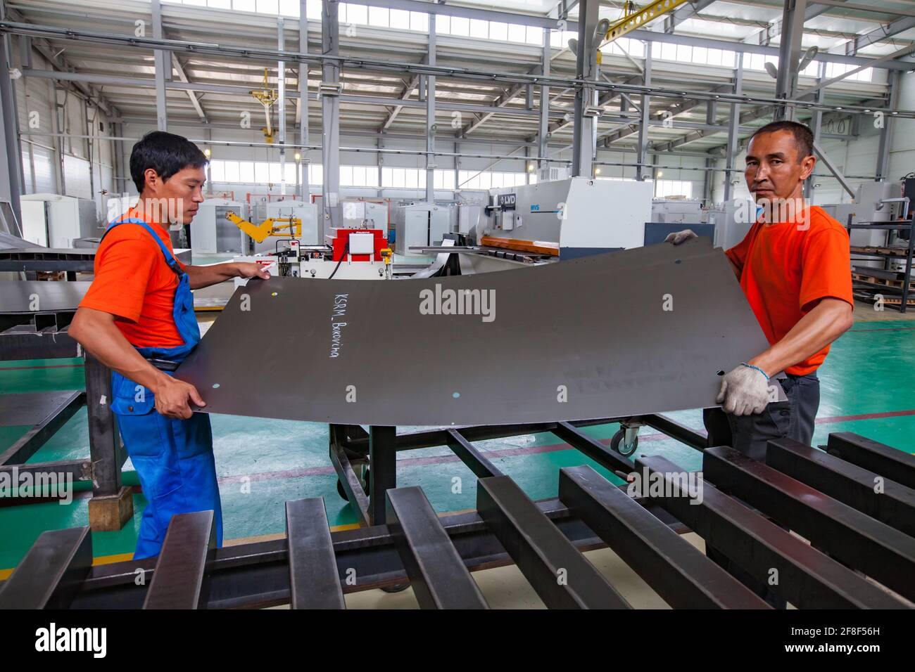 Aktau, Kazajstán. Dos trabajadores sostienen la chapa de metal. Máquina de corte láser CNC LVD en segundo plano. Producción de equipos eléctricos especiales. RIG Ltd Foto de stock