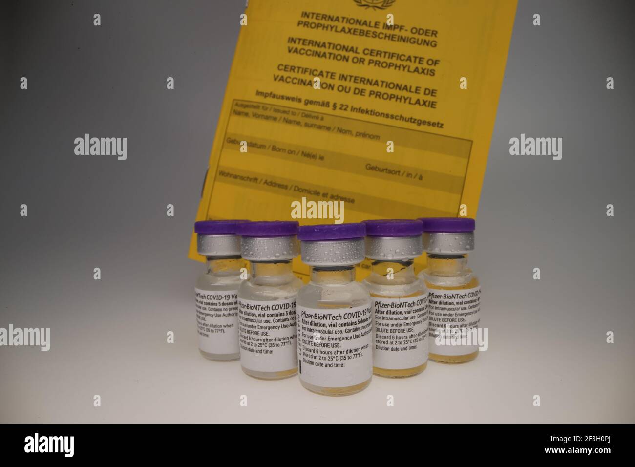 vial original de la vacuna de comirnaty dispuesto en un grupo en frente de un backrop blanco con certificado de vacunación detrás de ellos Foto de stock