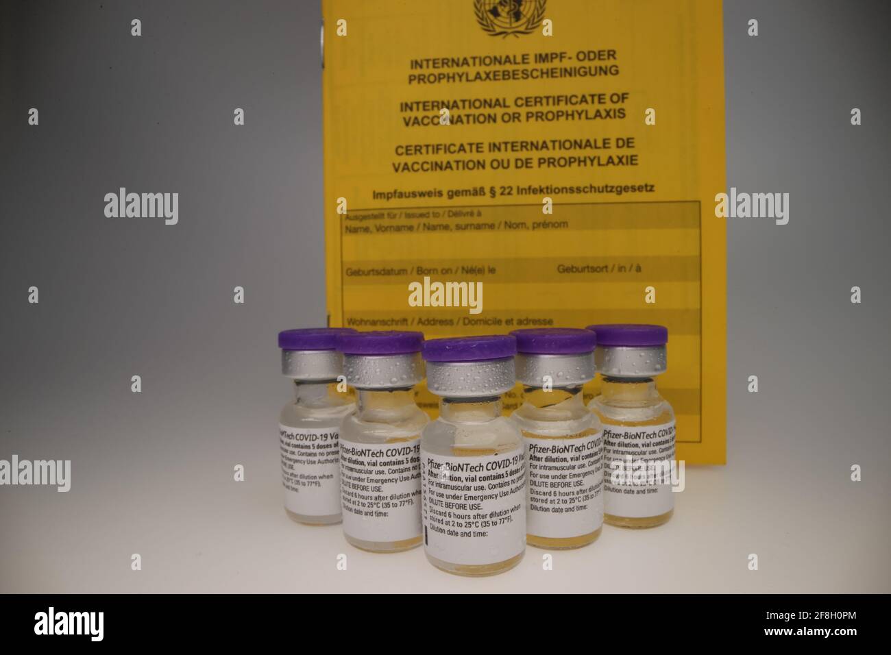 vial original de la vacuna de comirnaty dispuesto en un grupo en frente de un backrop blanco con certificado de vacunación detrás de ellos Foto de stock