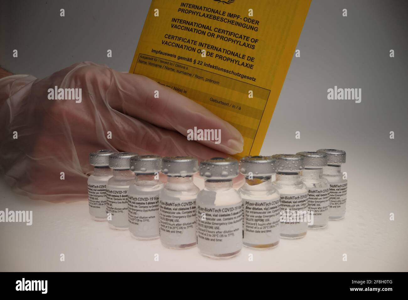 vial original de la vacuna de comirnaty dispuesto en un grupo en frente de un backrop blanco con un certificado de vacunación detrás de ellos Foto de stock