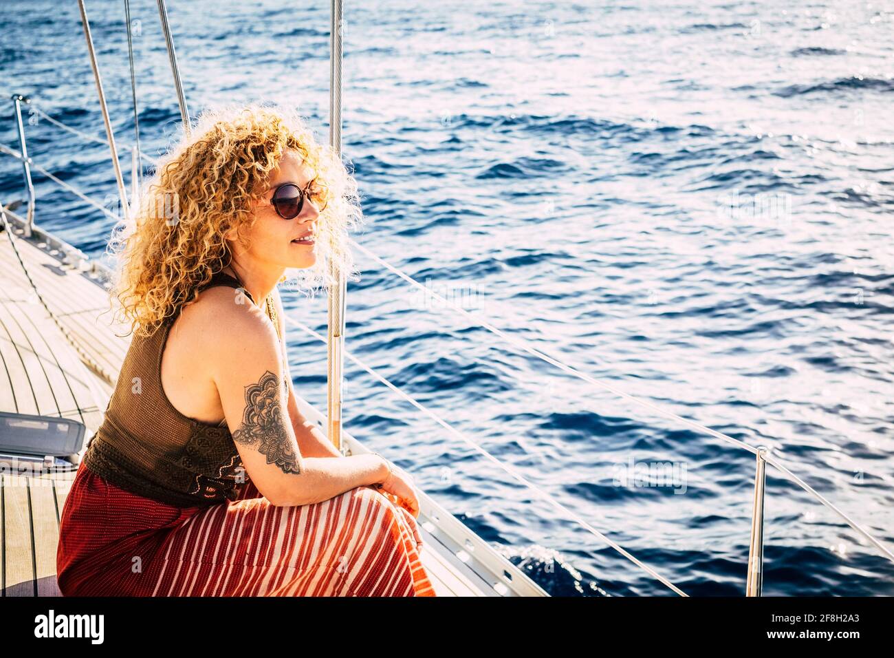 Alegre atractiva joven adulta rubia sonrisa y disfrutar de la excursión sentado en la cubierta del barco con vista al azul mar alrededor - concepto de Foto de stock