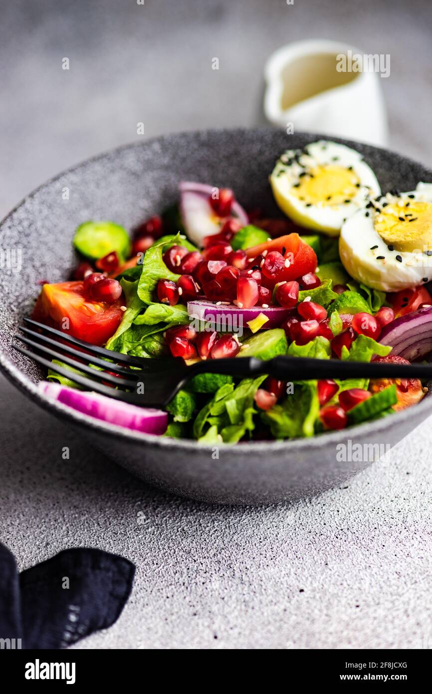 Ensalada con lechuga, tomate, cebolla roja, semillas de granada y huevo duro con semillas de sésamo Foto de stock