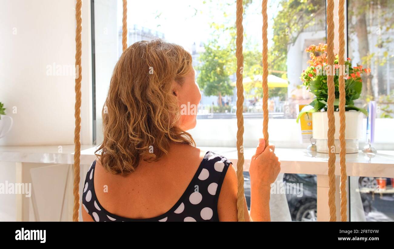 mujer va a conducir en un columpio cerca de un café en un día soleado. El  concepto de libertad, hacer deseos y hacer realidad los sueños, la tristeza  y el pensamiento Fotografía