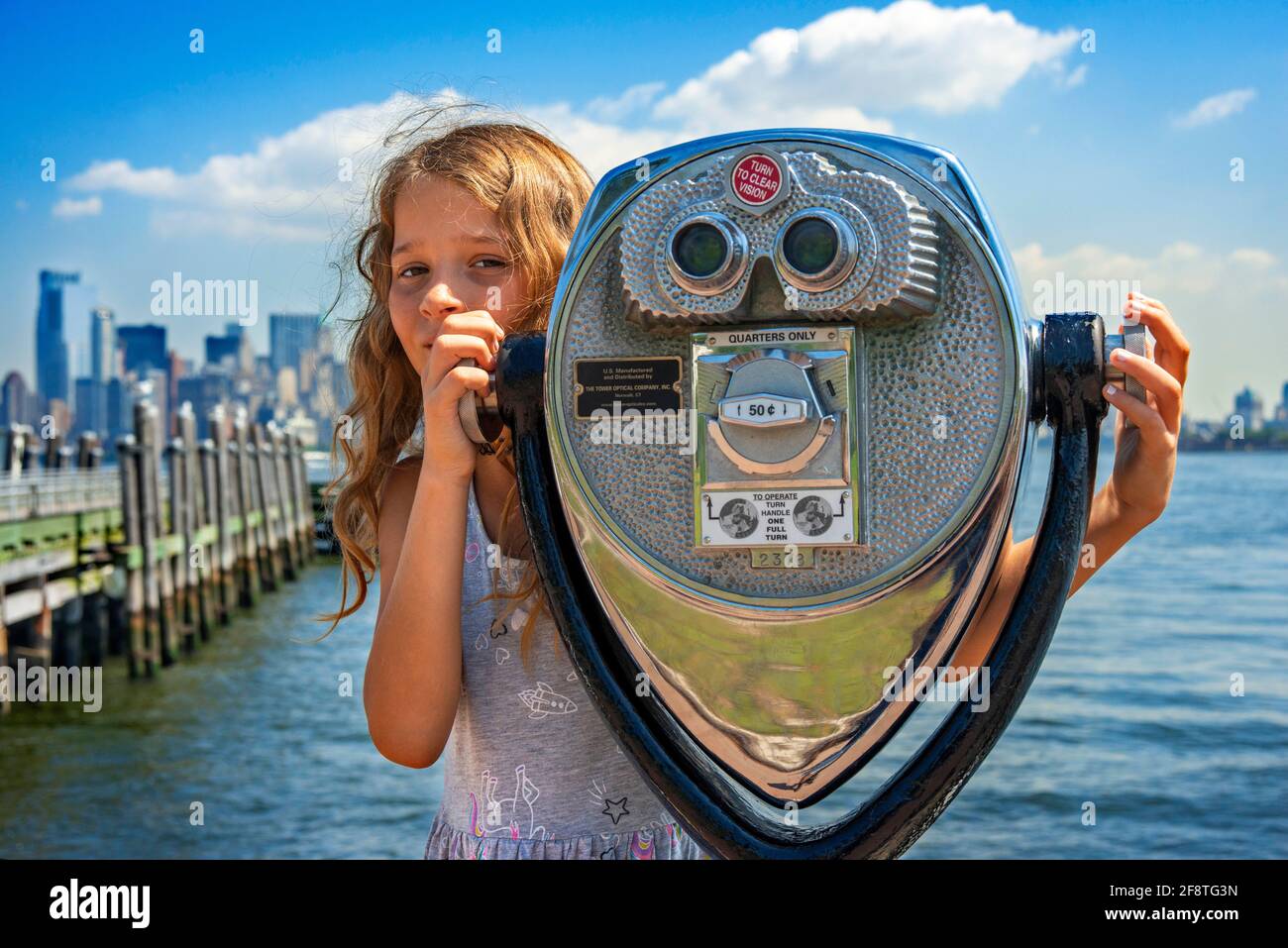 Chica de turismo con prismáticos en la isla de Ellis con el Manhattan Vistas de la parte trasera de Nueva York Foto de stock