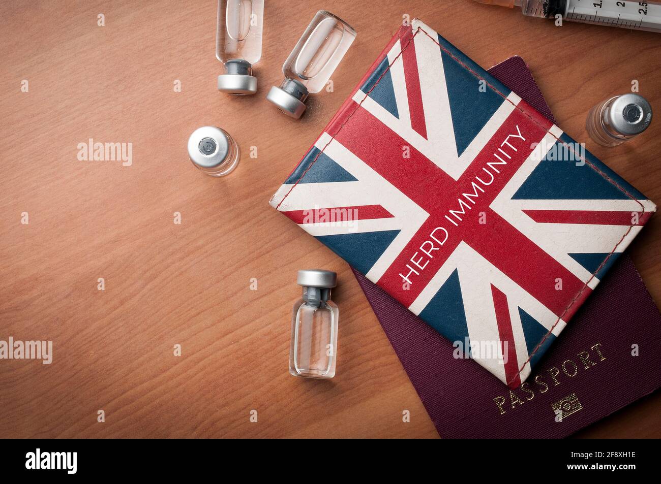 Concepto de inmunidad de rebaño: Cartera con bandera británica sobre un pasaporte junto con algunos viales de vacuna y una jeringa sobre una mesa de madera Foto de stock