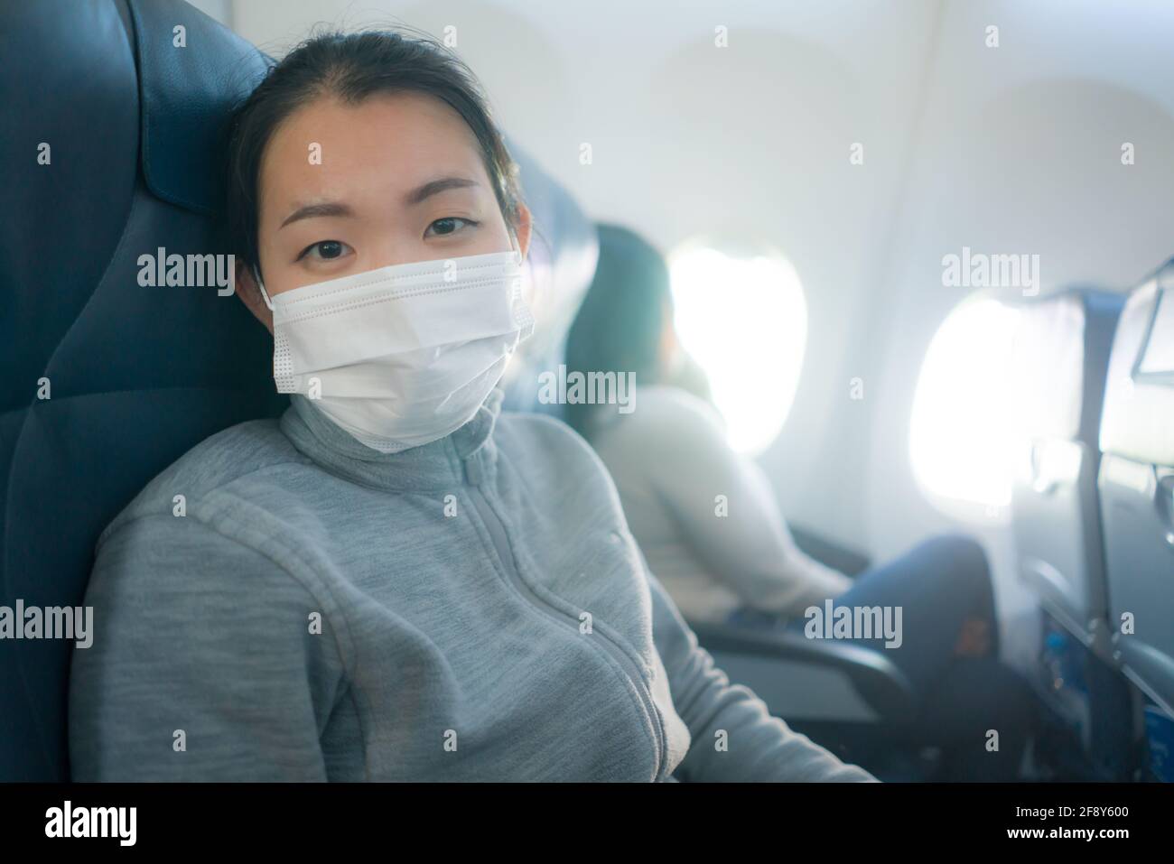 Mujer turística asiática volando en tiempos de covid19 - joven Feliz y emocionada chica coreana con máscara sentada cabina de avión lista para mirar vuelo Foto de stock