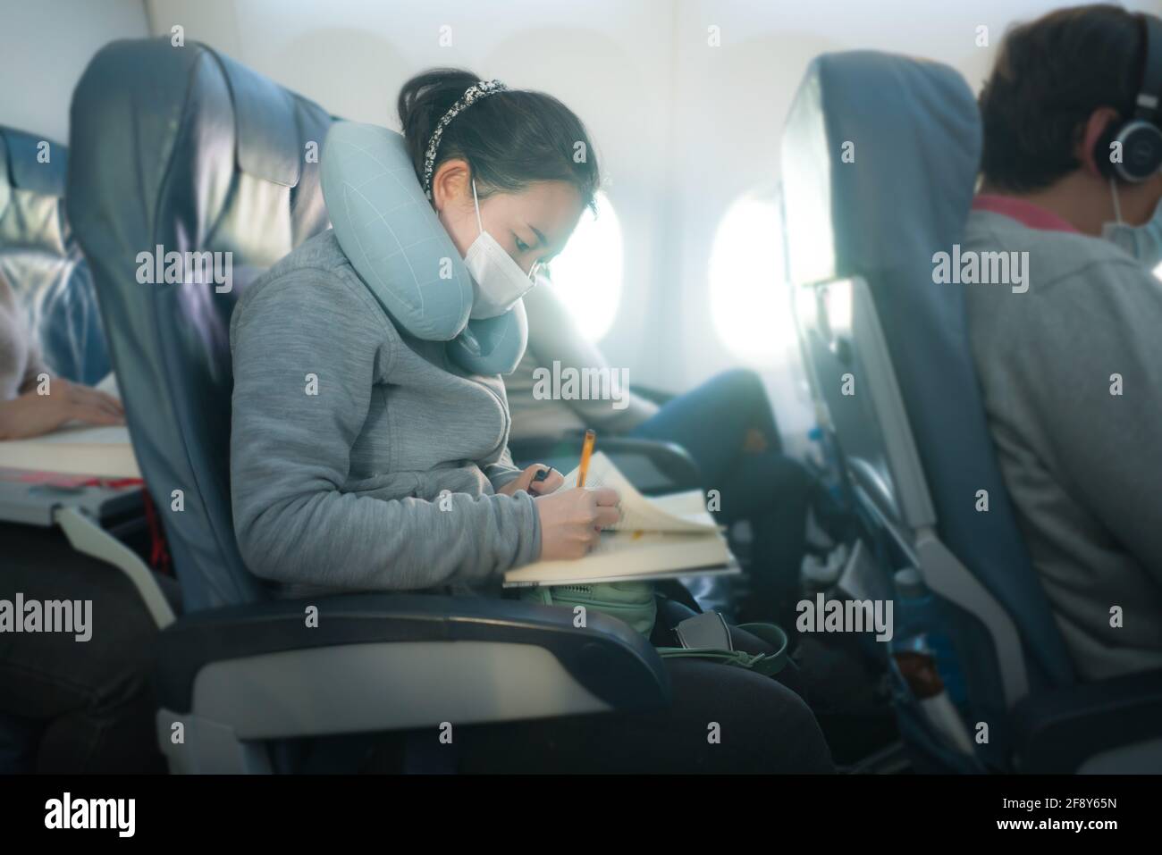 volando en tiempos de covid19 - joven dulce y lindo Mujer coreana asiática con máscara sentada en la cabina del avión leer libro o novela disfrutando del vuelo Foto de stock