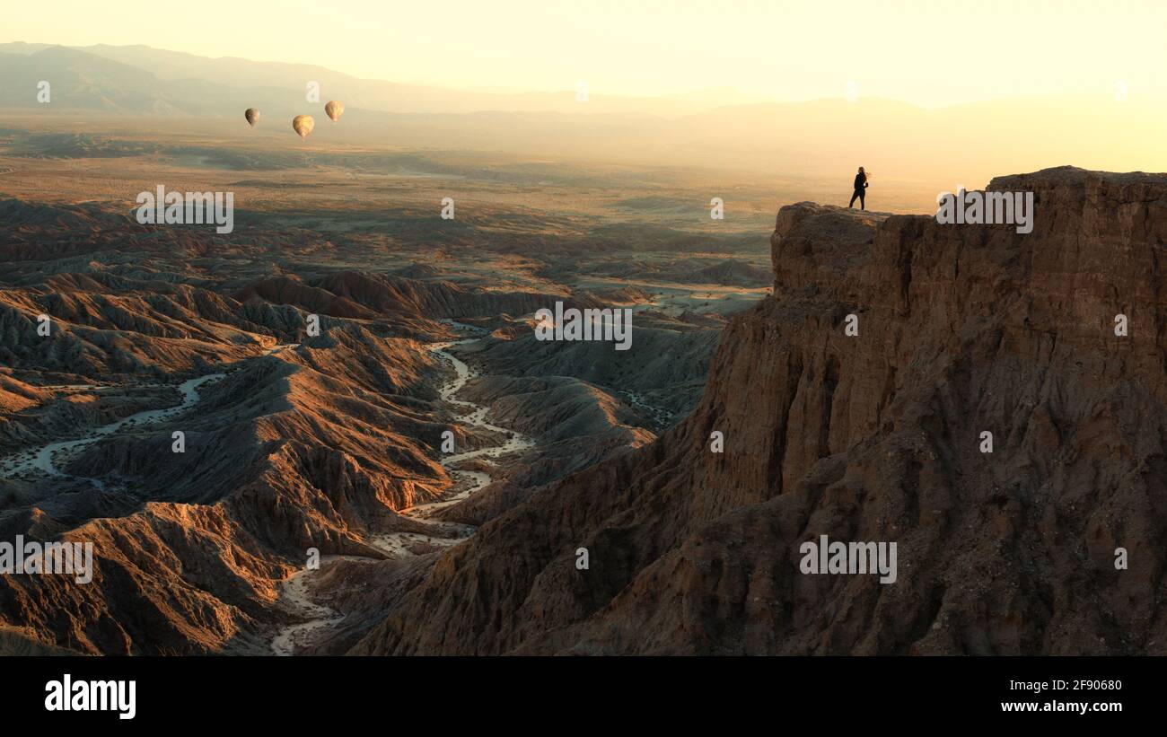 Mujer de pie en Font's Point mirando globos aerostáticos volando sobre tierras de badlands, Anza-Borrego Desert State Park, California, Estados Unidos Foto de stock