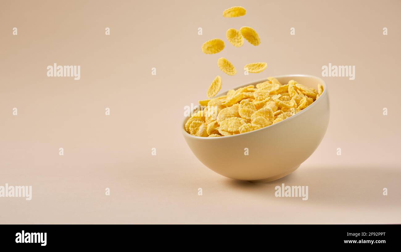 Desayuno tradicional con cereales. Copos de maíz cayendo en un tazón sobre un fondo beige claro. Foto de stock