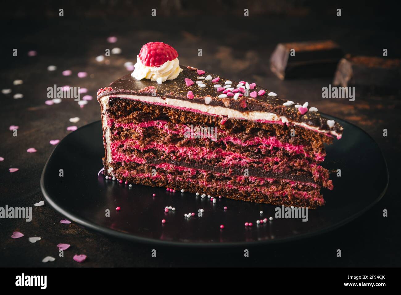 Pieza de torta de chocolate de frambuesa sobre un plato negro fondo marrón oscuro Foto de stock