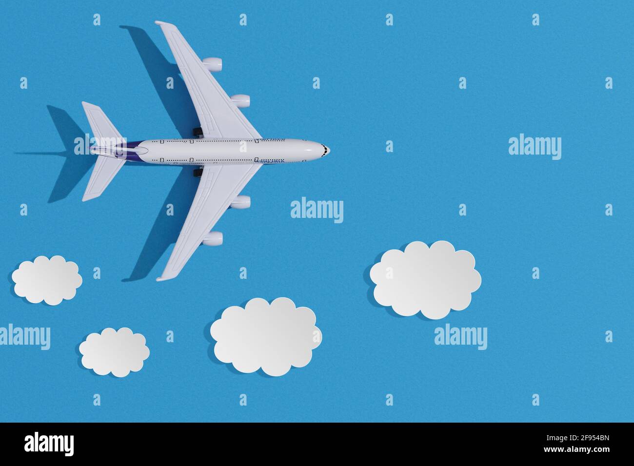 Avión de juguete en miniatura sobre fondo de papel de colores. Diseño plano de concepto de viaje con plano y nubes sobre cielo azul con espacio de copia. Foto de stock