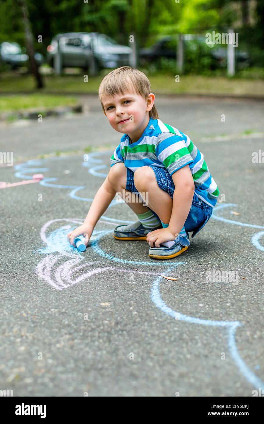 Lindo niño y niña dibujando con tiza en la acera en el parque. Actividades  de verano para niños. Dibujo creativo de un niño con tiza azul en la r  Fotografía de stock -