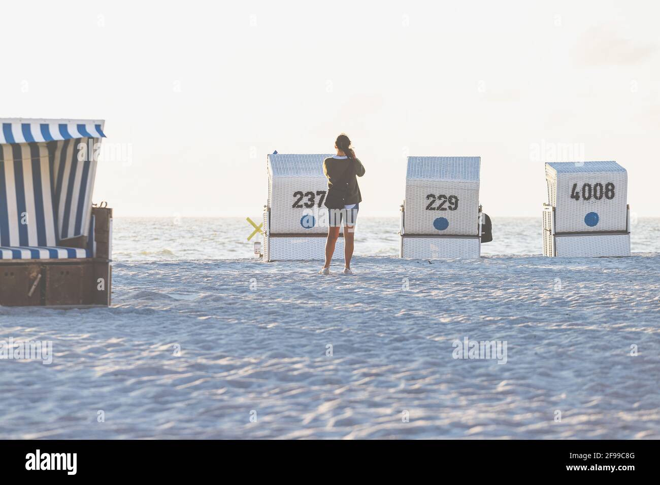 Una mujer toma una foto con un teléfono celular de una escena en la playa - va a ser puesta de sol. Foto de stock