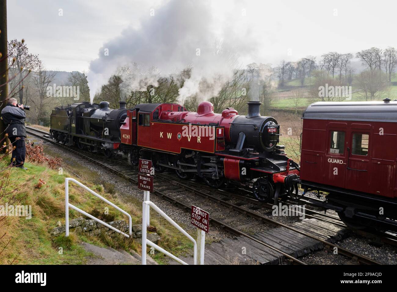 Los trenes de vapor históricos (locos) que soplaban nubes de humo se detuvieron en el cruce (hombre tomando foto en tierra) - ferrocarril de herencia, KWVR, Yorkshire, Inglaterra, Reino Unido. Foto de stock