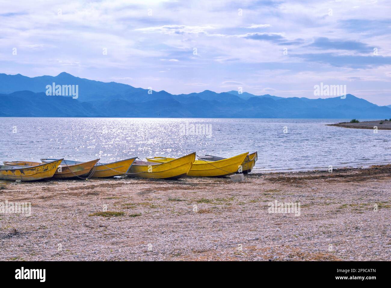 Hermoso paisaje veraniego con costa de lago - viejos barcos amarillos, cielo azul y montañas en el horizonte. Foto de stock