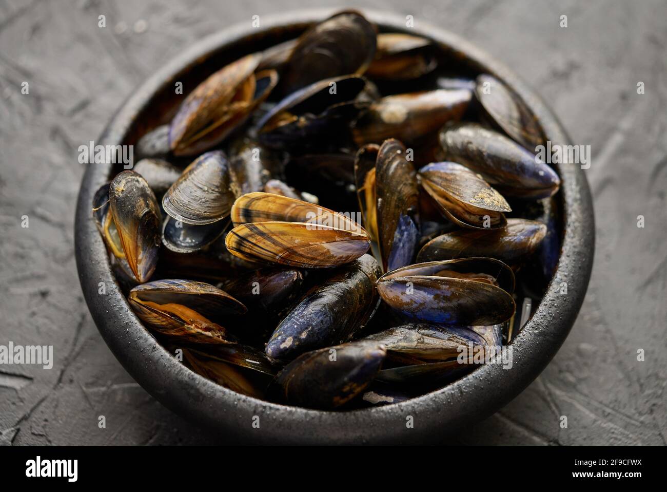 Mejillones de mar frescos y crudos en un tazón de cerámica negro sobre fondo de piedra oscura Foto de stock