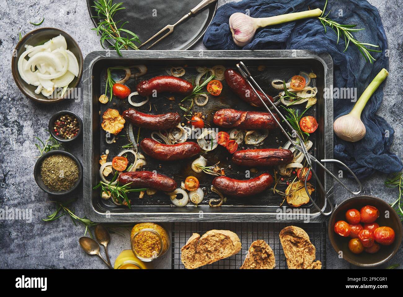 Vista superior de las deliciosas salchichas a la parrilla servidas con cebolla, tomates, ajo, pan y hierbas Foto de stock