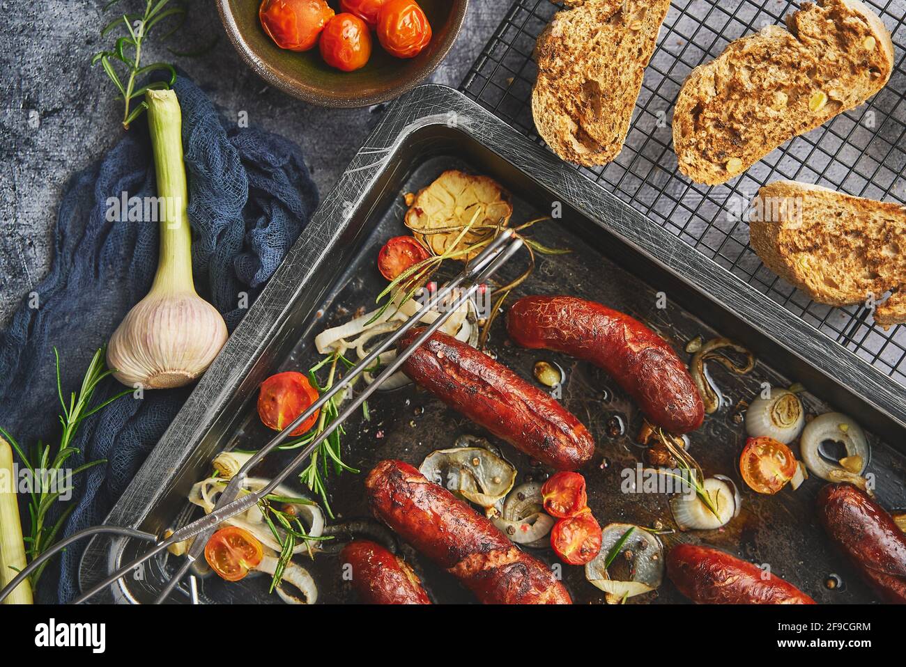 Sabrosas salchichas caseras de romero a la parrilla colocadas en una bandeja de freír de hierro sobre mesa rústica de piedra oscura Foto de stock