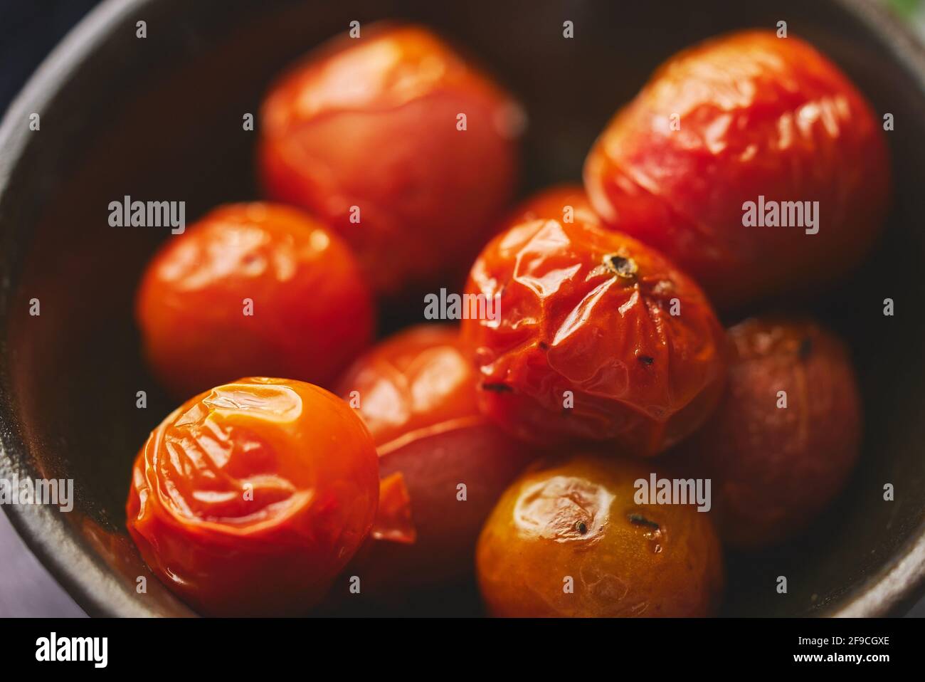 Tomates cherry asados colocados en un cuenco cerámico oscuro. Primer plano de la macro. Foto de stock