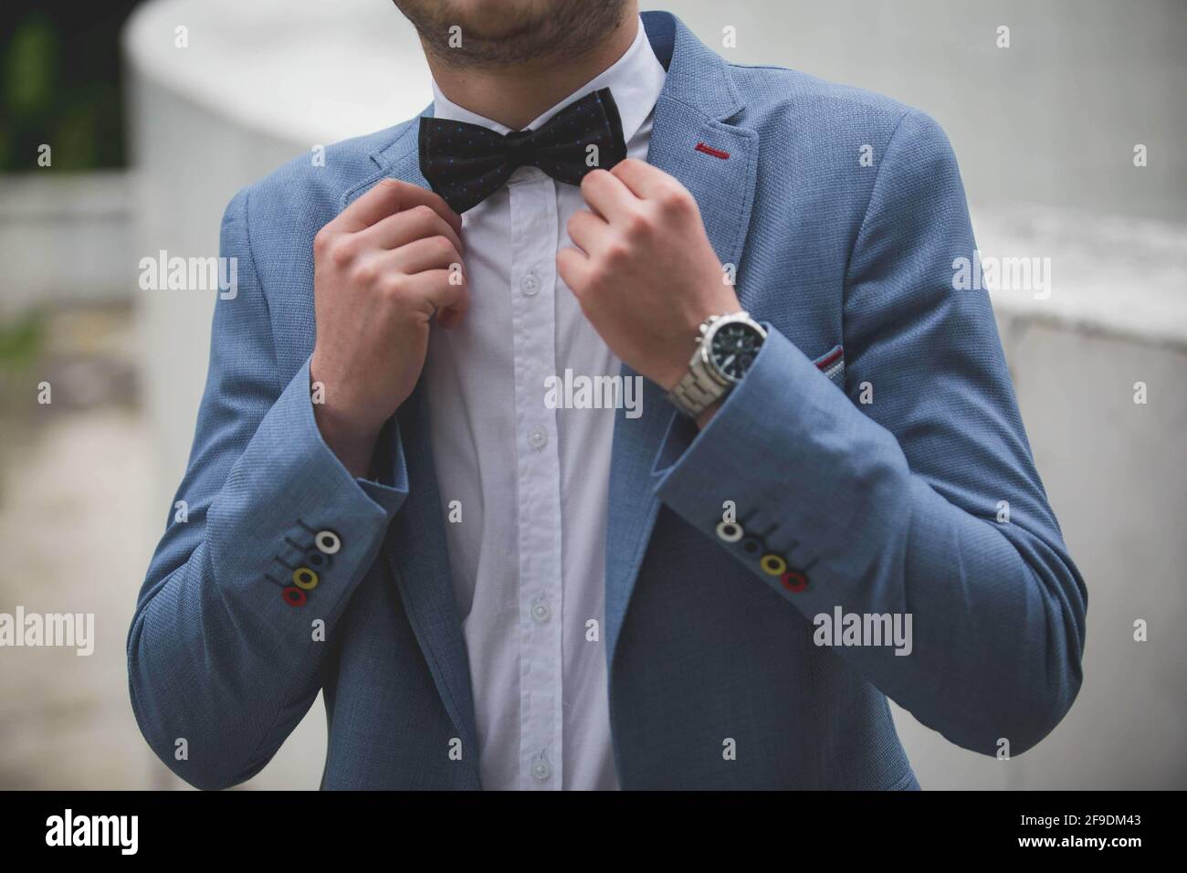 Una sección media de un novio que fija su pajarita negra que usa traje azul  con botones en las mangas de colores Fotografía de stock - Alamy