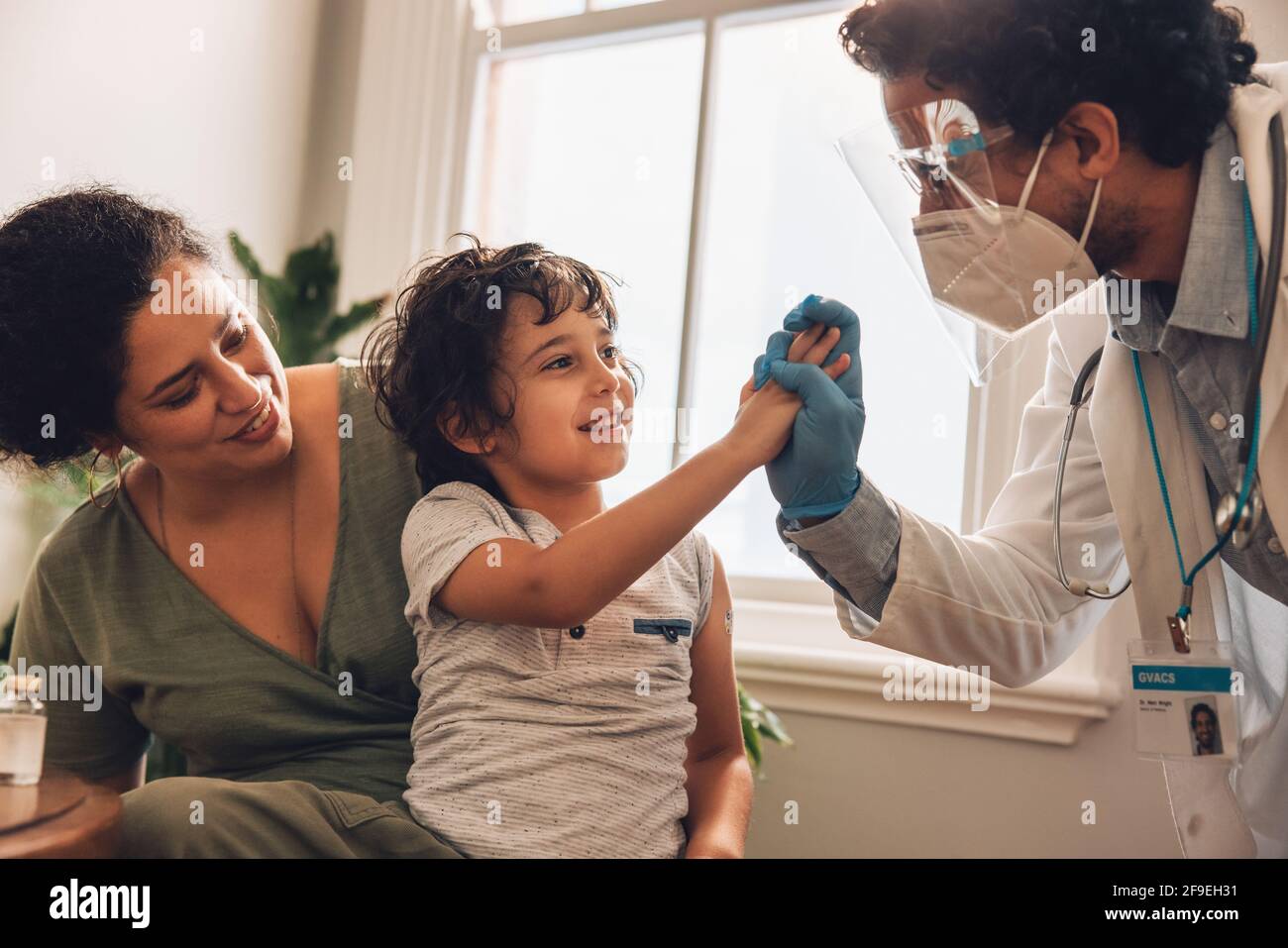 El médico y el niño se dan cinco dosis altas después de la vacunación. La madre y el hijo en casa reciben la vacuna durante la pandemia. Foto de stock