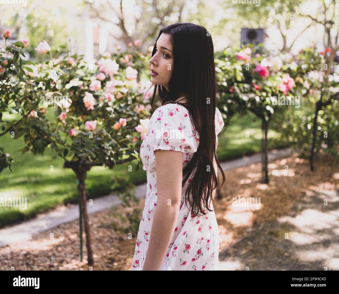 Hermosa Latina adolescente admirando las rosas en un jardín en la luz vestido de primavera Foto de stock