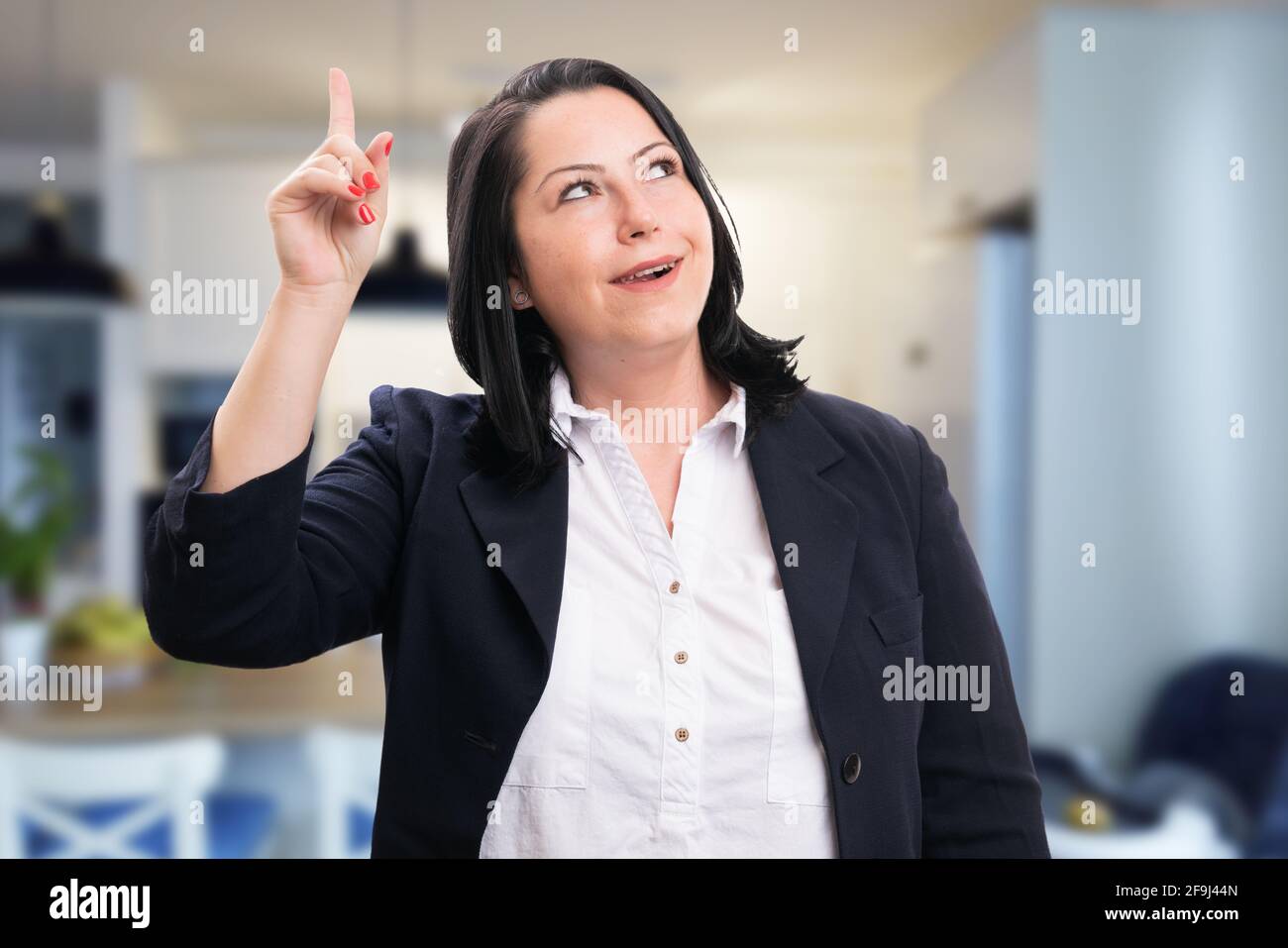 Alegre adulto corporativo mujer de negocios con elegante sport traje hacer gesto de buena idea con el dedo sobre el fondo de la habitación Foto de stock