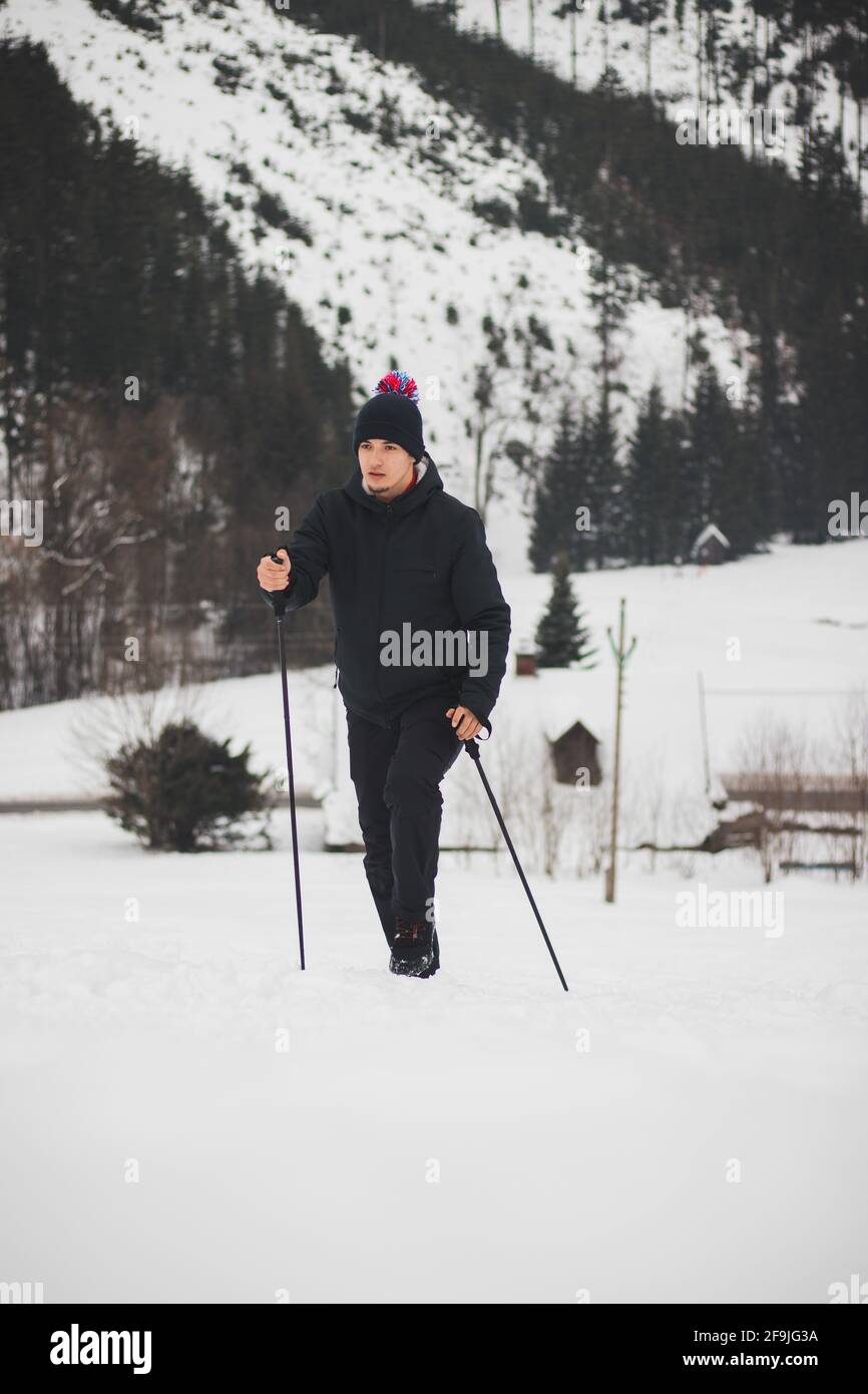 hombre en invierno la ropa sube la pista de esquí a la cima con la ayuda de postes de escalada una mejor estabilidad más fácil subir a las montañas.