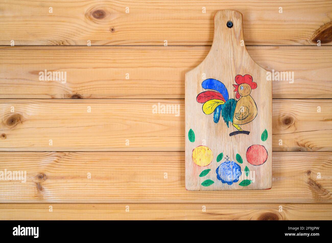 tabla de corte vieja con madera quemada y dibujo coloreado un gallo cuelga  en un clavo en la pared de madera de tablón. artesanía de bricolaje para  niños Fotografía de stock 