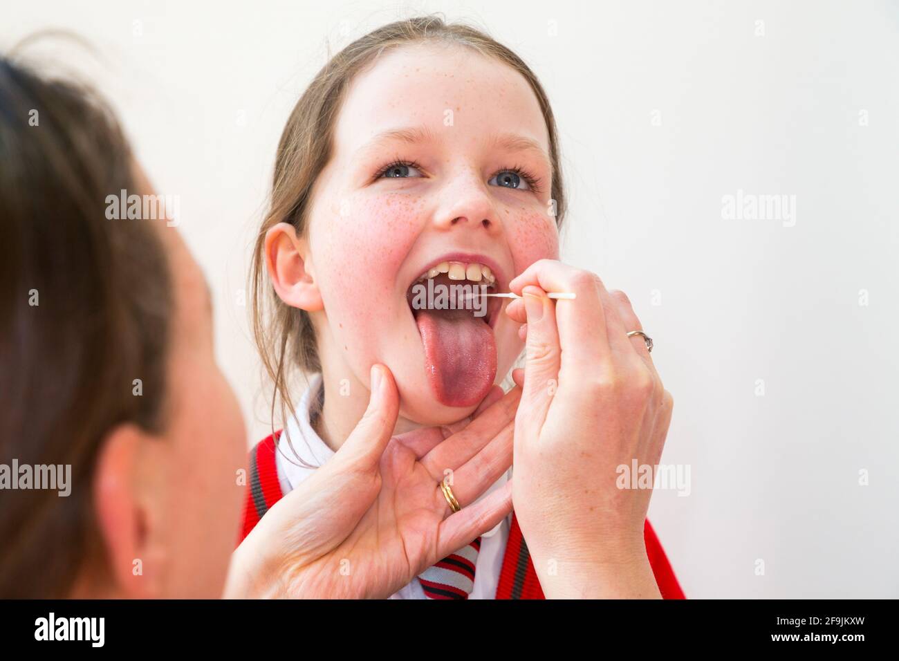 Edad escolar niño niño escuela primaria niña de nueve años / 9 años de edad que toma muestras de su garganta para su uso en una prueba de flujo lateral LFT de la empresa china Innova. Inglaterra Reino Unido. (123) Foto de stock
