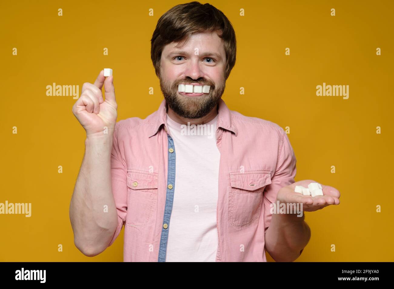 Un hombre gracioso puso trozos de azúcar en la boca como si fueran dientes y sonrisas. Fondo amarillo. Foto de stock