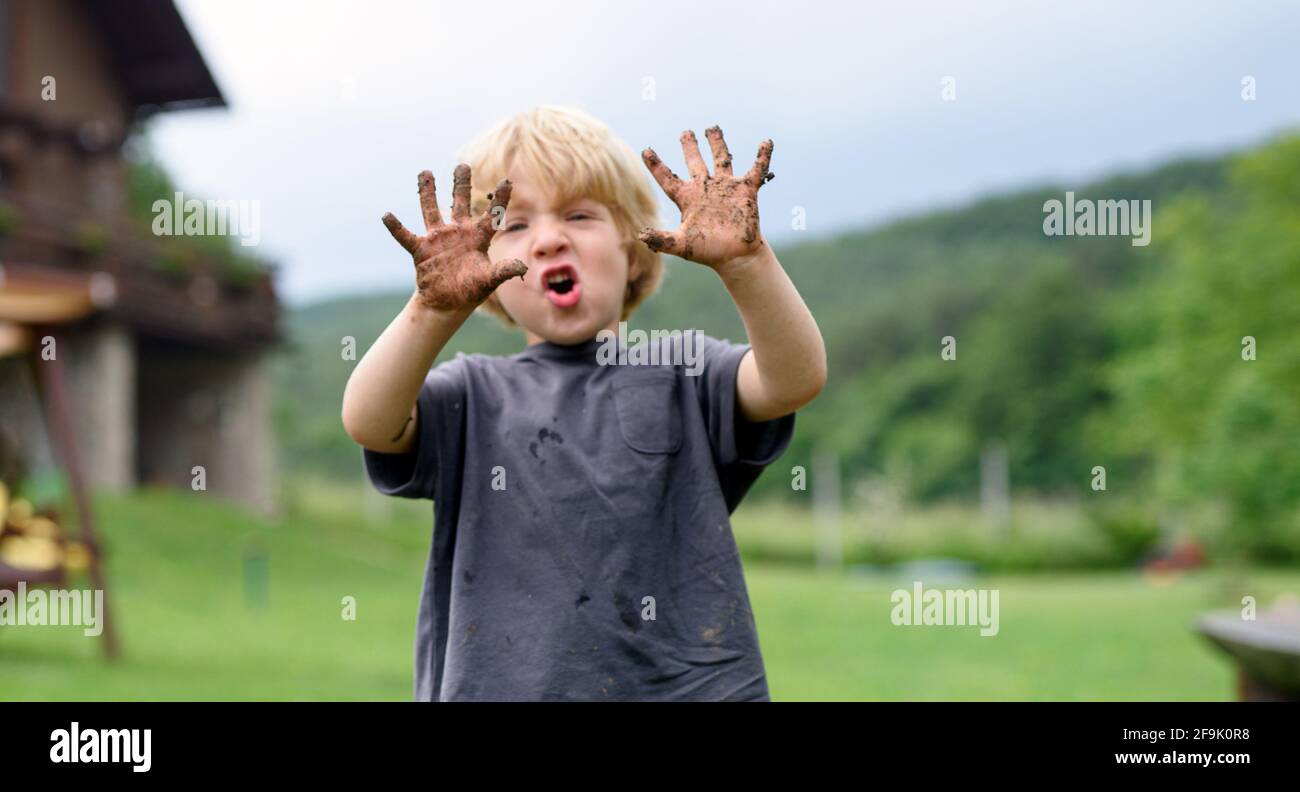 Niño pequeño con las manos sucias de pie en el jardín vegetal, estilo de vida sostenible. Foto de stock