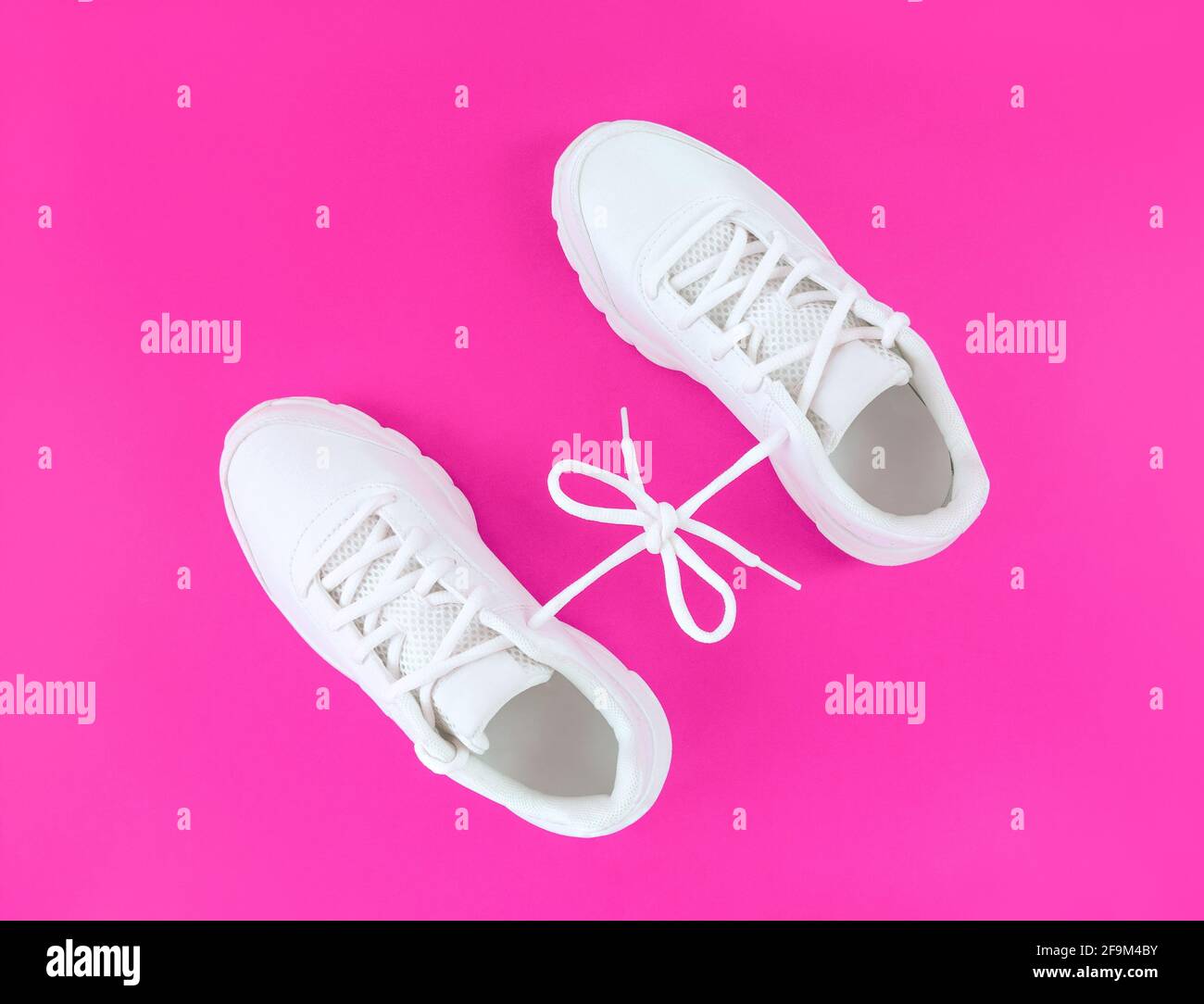 deportivas blancas conectadas con lazo de cordones sobre fondo rosa Fotografía de stock - Alamy