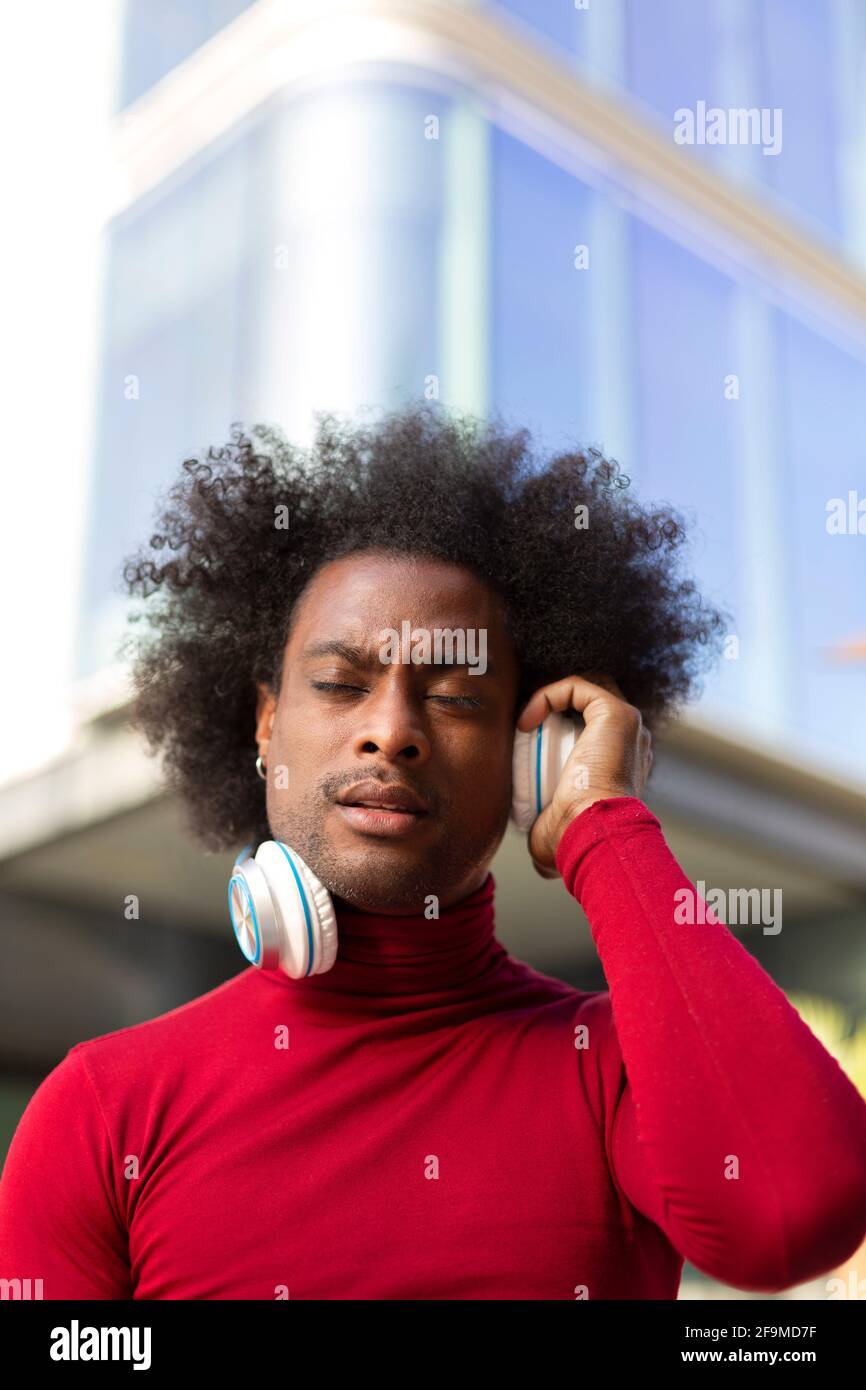 Retrato de un hombre negro joven con peinado afro escuchando música al aire libre. Espacio para texto. Foto de stock